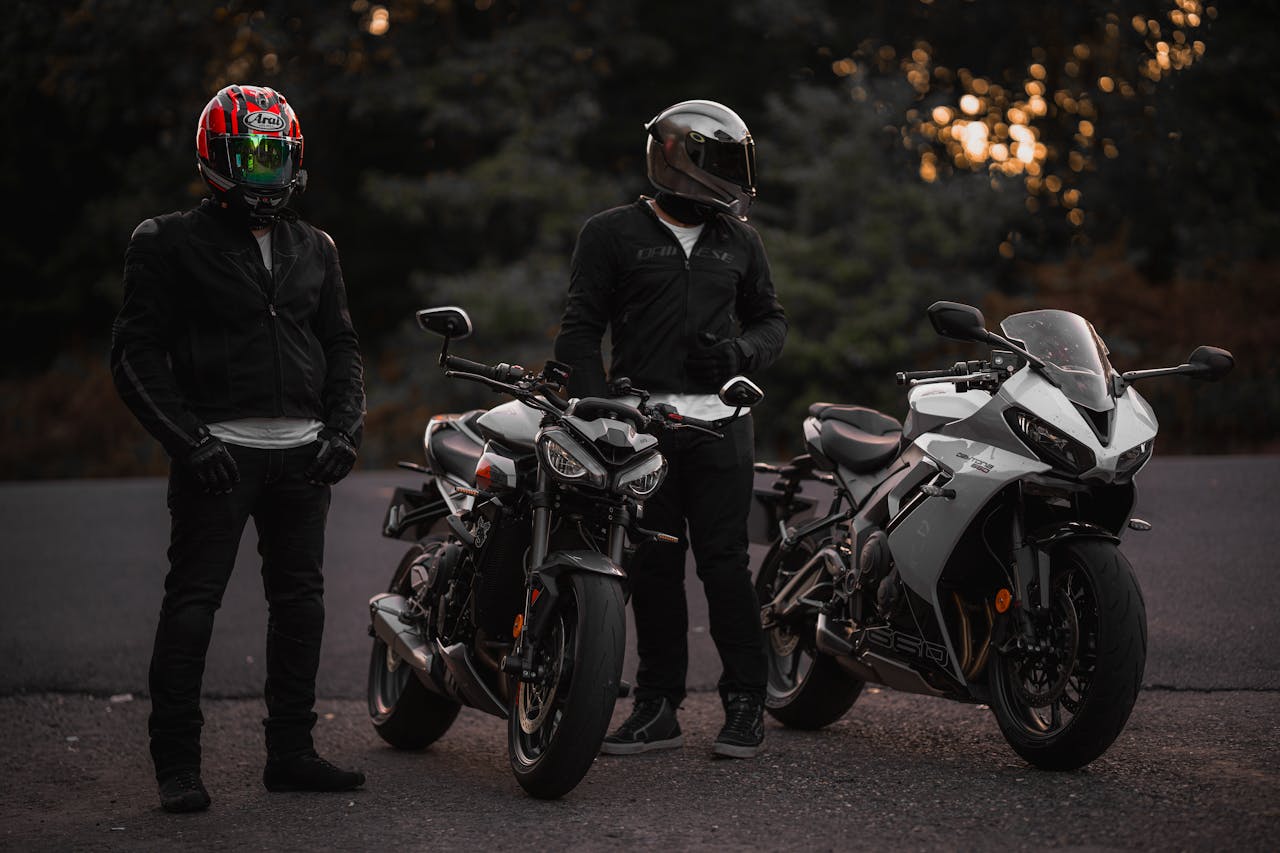 Two bikers with helmets standing beside their sport motorcycles during twilight on a road.